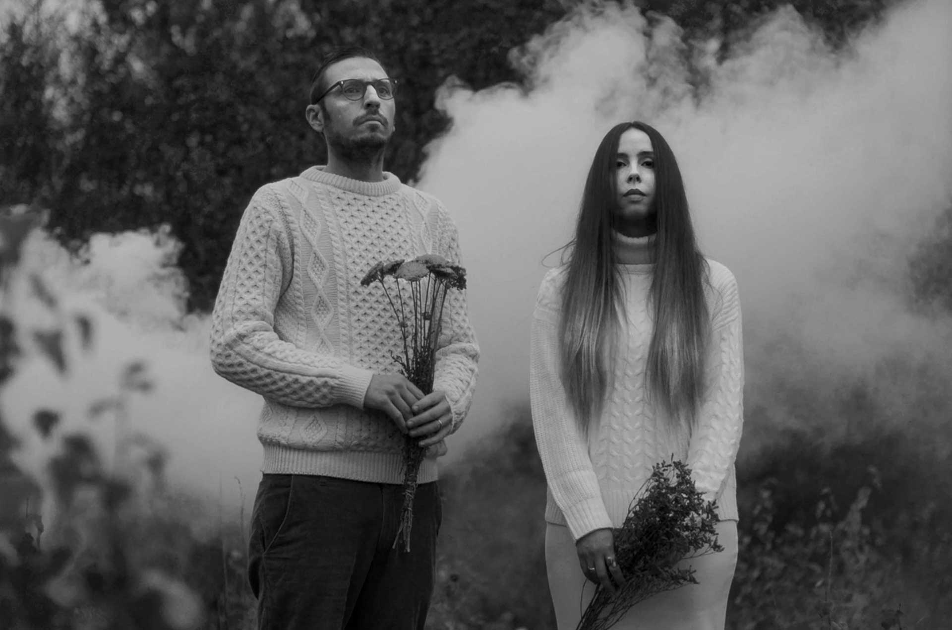 music band of men and woman standing in front of smoke holding flowers in black and white