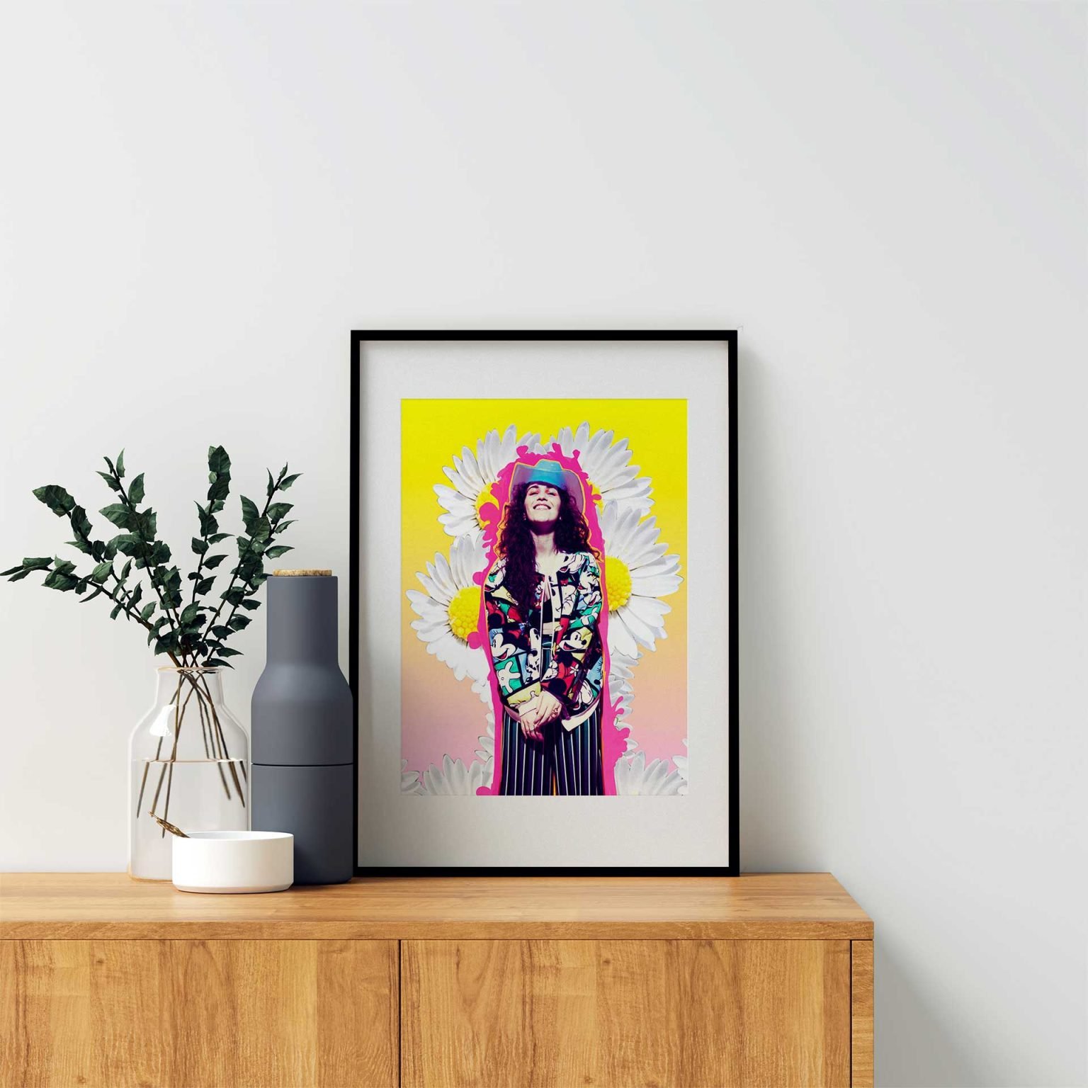 A vibrant framed artwork featuring a fashion-forward portrait set against a bold yellow and pink background with oversized daisies. The subject exudes confidence and individuality, wearing a colorful patterned jacket and striped trousers, topped with a blue cap. A statement piece celebrating creativity and self-expression.