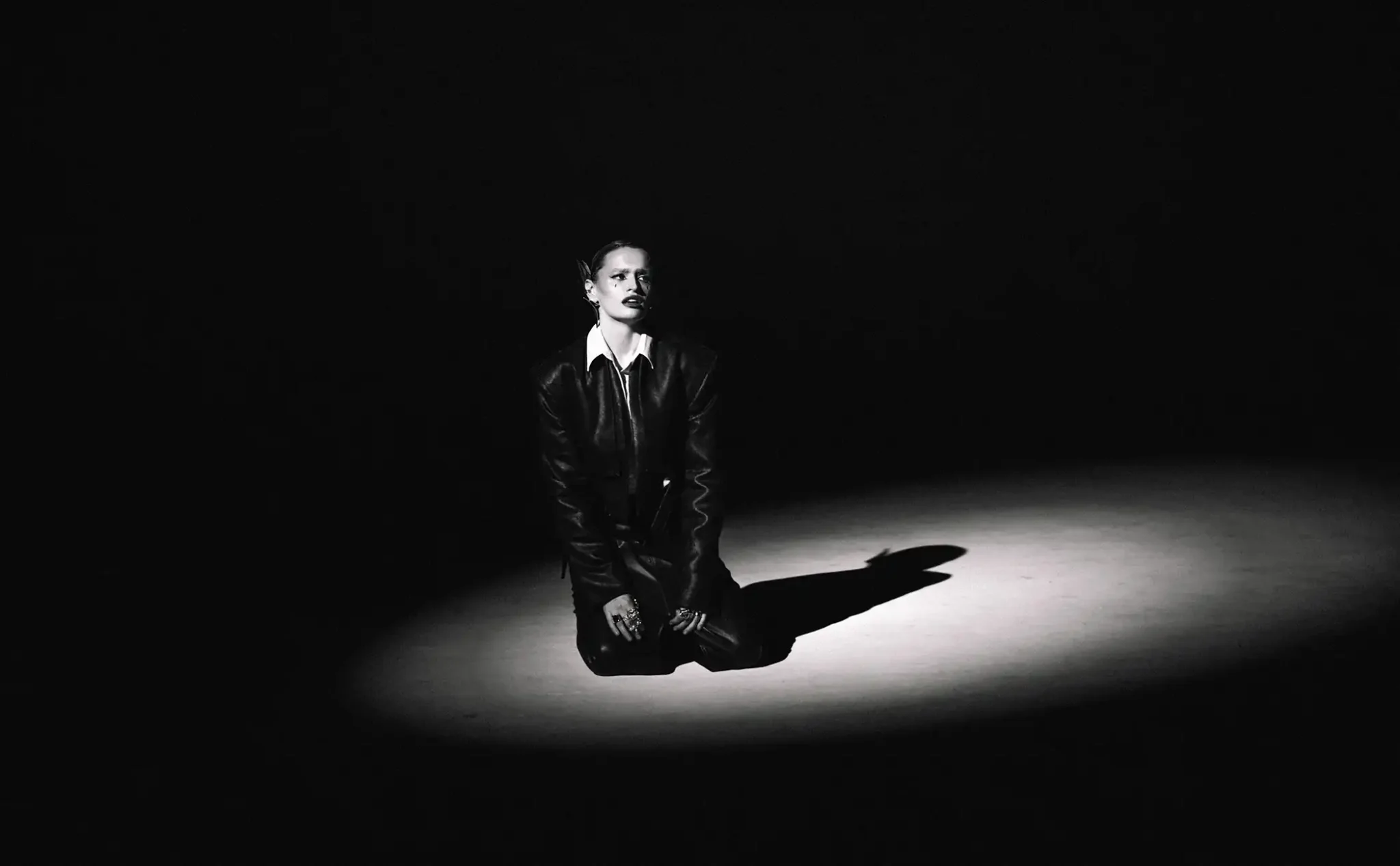 Black and white photo of Katia Pojidaeva kneeling alone in a spotlight.