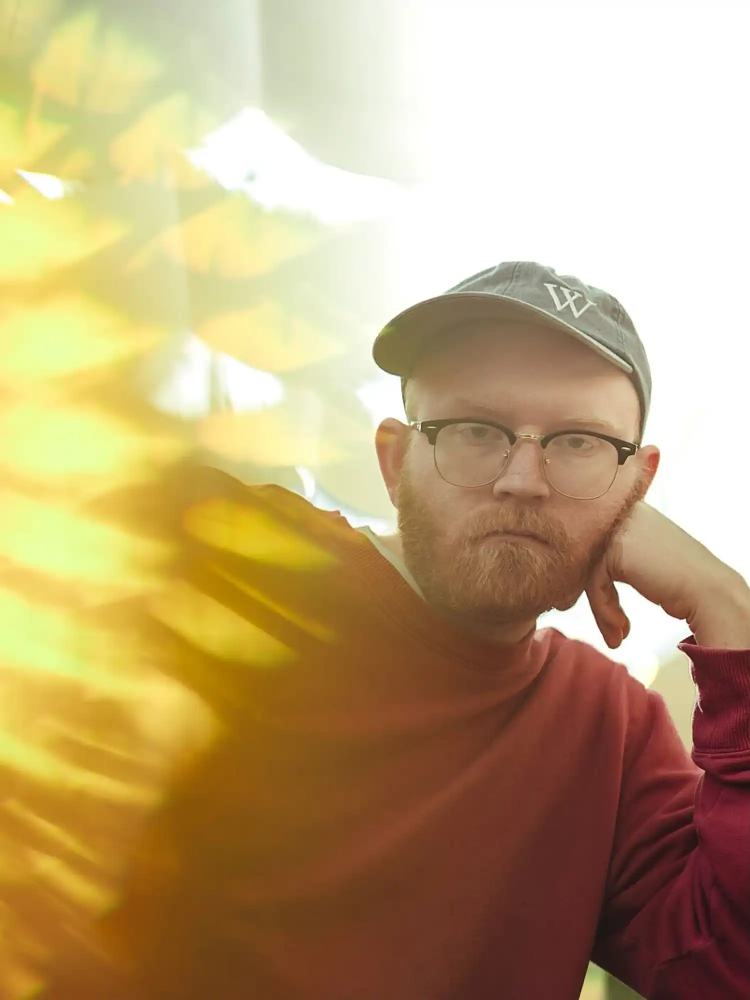 Noah Lefgren in a red sweater and cap, resting chin on hand in sunlit portrait
