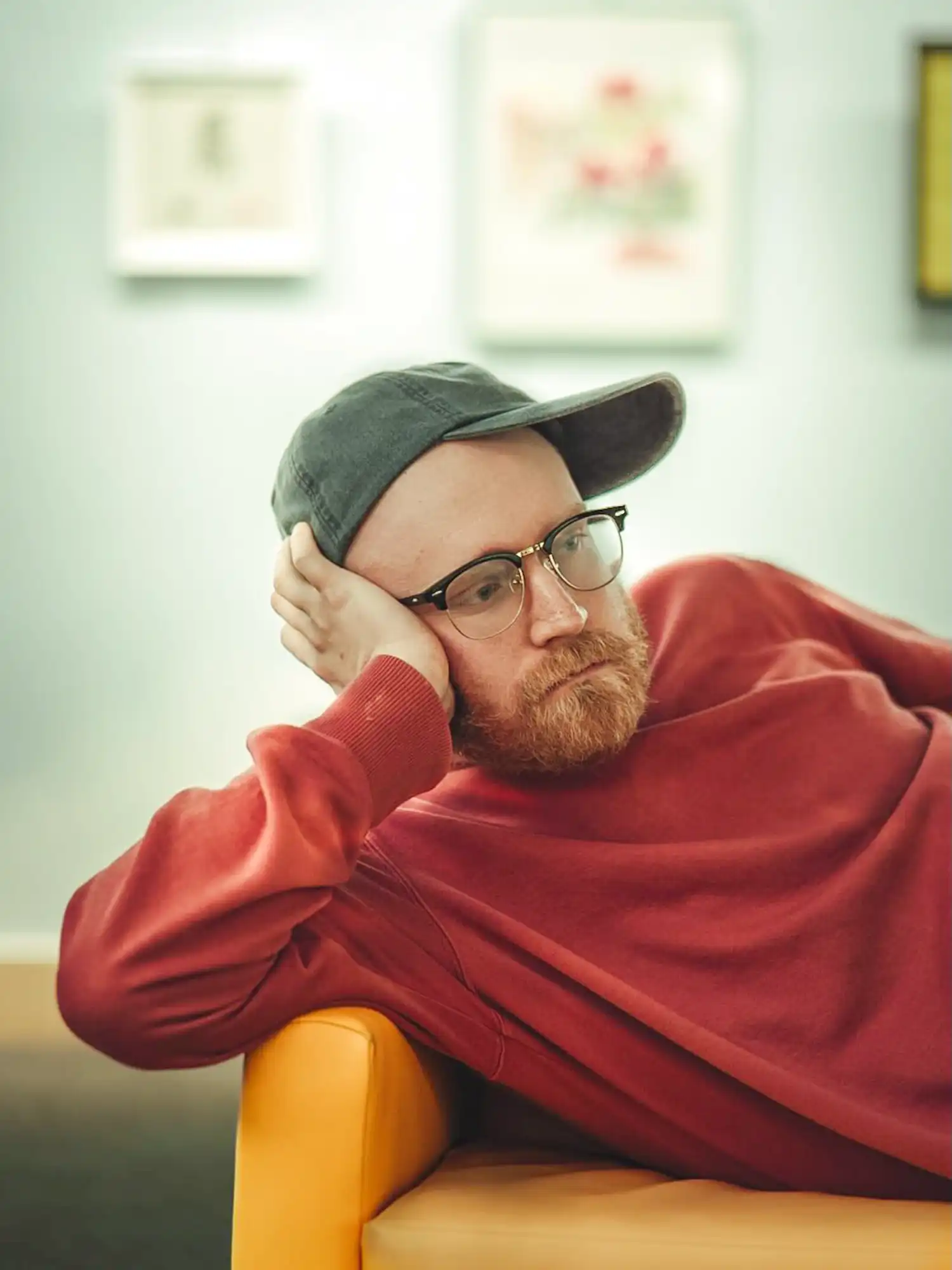 Noah Lefgren seated in a yellow chair, red sweater and cap, resting head on hand